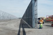 Two workers installing a gate in a long fence line on a sunny day