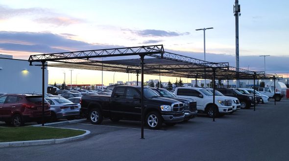 A parking lot with vehicles parked under a metal canopy structure at sunset