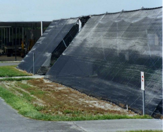 Large black mesh wind fence installed on a grassy slope near a paved path