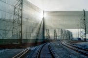 Railway tracks curve beside tall, translucent wind fences with sunlight filtering through