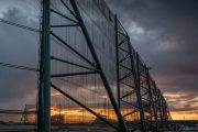 A large industrial fence structure with a sunset visible through its mesh panels
