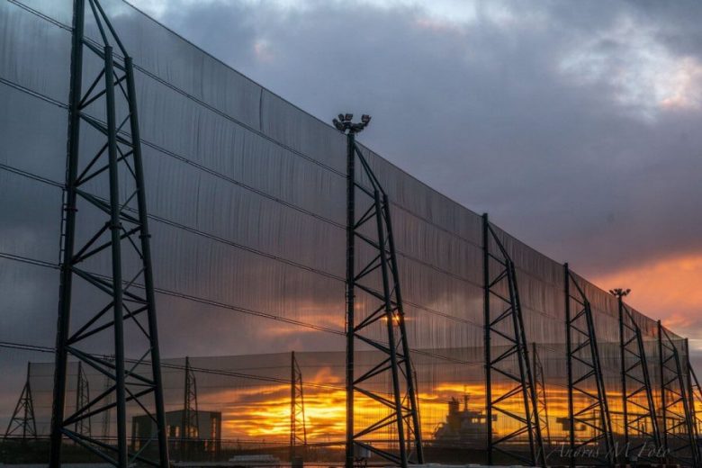 A tall metal fence structure with netting against a dramatic sunset sky