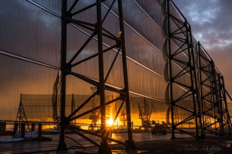 A large industrial structure with translucent panels stands against a vibrant sunset