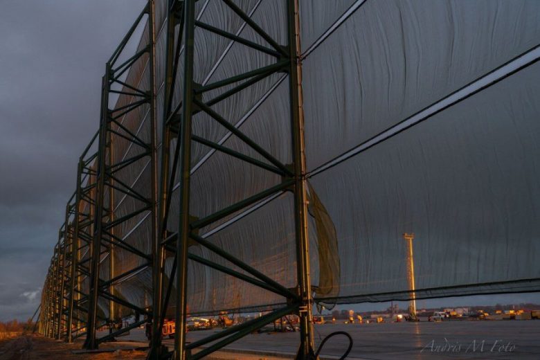 A large industrial wind fence structure stands against a dark, cloudy sky