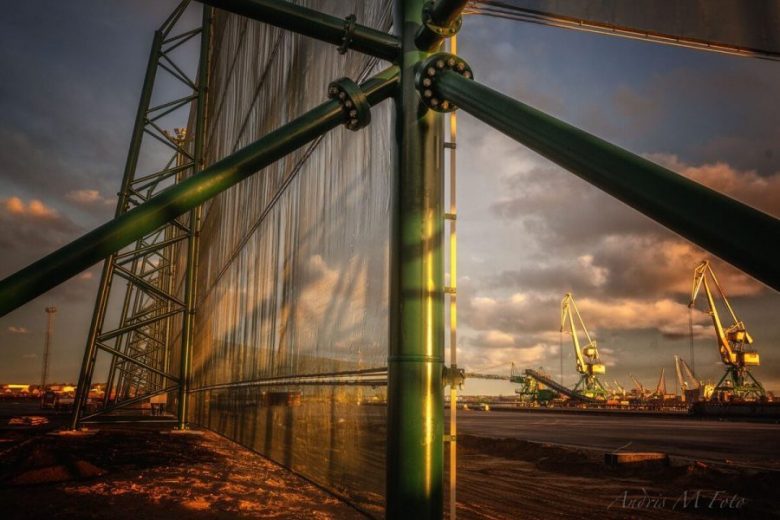 A large industrial wind fence with cranes in the background at sunset