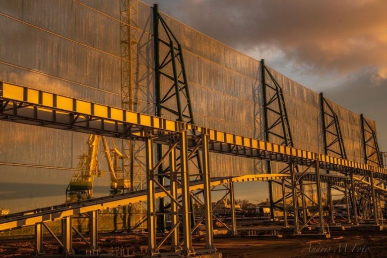 Large industrial structure with metal framework and mesh panels, set against a sunset sky