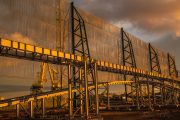 A large industrial structure with metal framework and translucent panels, reflecting a sunset