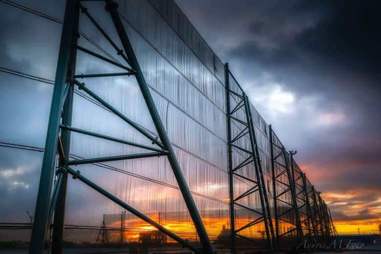 A large industrial fence structure against a dramatic sunset sky