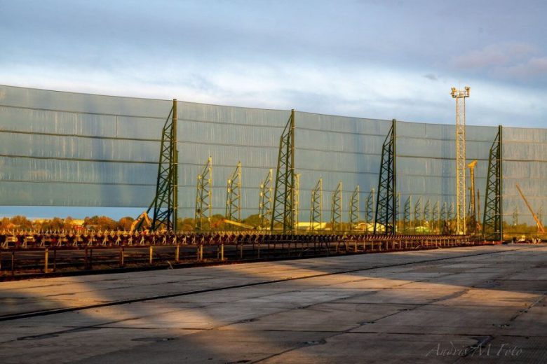 A long industrial wind fence stretches across a paved area with metal supports