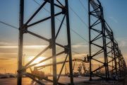 A large metal structure with workers on a lift against a sunset backdrop