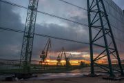 Cranes silhouetted against a sunset, viewed through a mesh fence with metal supports