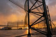 A large wind fence structure stands against a dramatic sunset sky