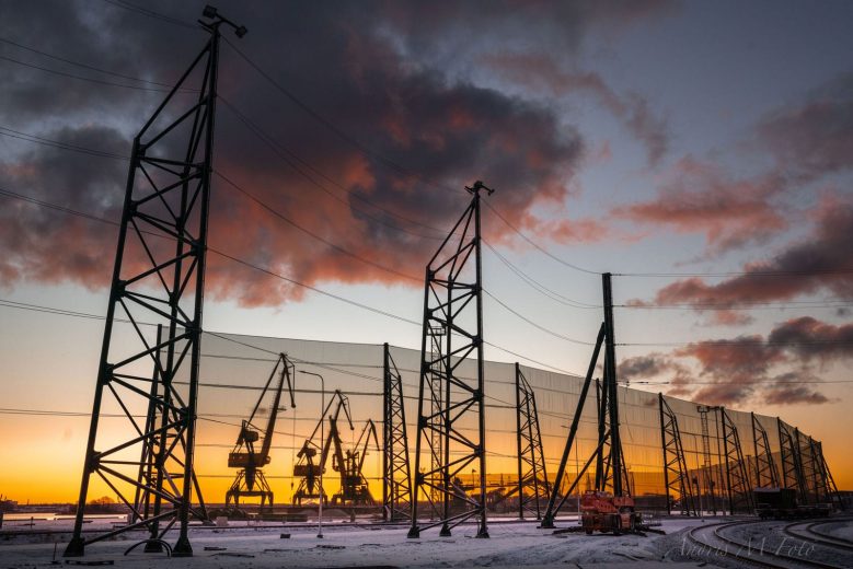 Industrial cranes and wind fences silhouetted against a vibrant sunset sky