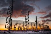 Industrial wind fences stand against a dramatic sunset with silhouetted cranes in the background
