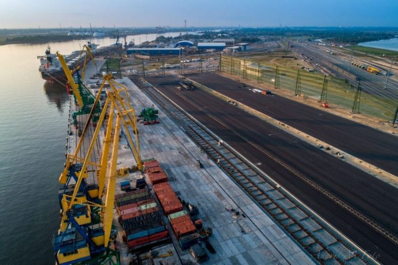 Aerial view of a port with cranes, shipping containers, and adjacent railway tracks