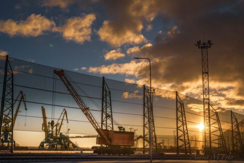 A construction site with cranes and a large fence against a sunset sky