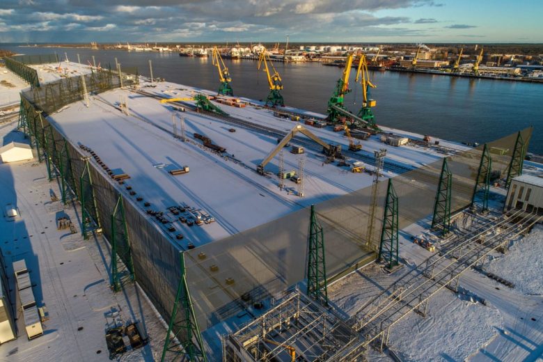 An aerial view of a snowy industrial site with cranes and wind fences by the water