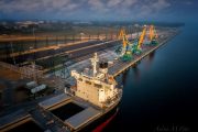 Aerial view of a cargo ship docked at an industrial port with cranes and infrastructure