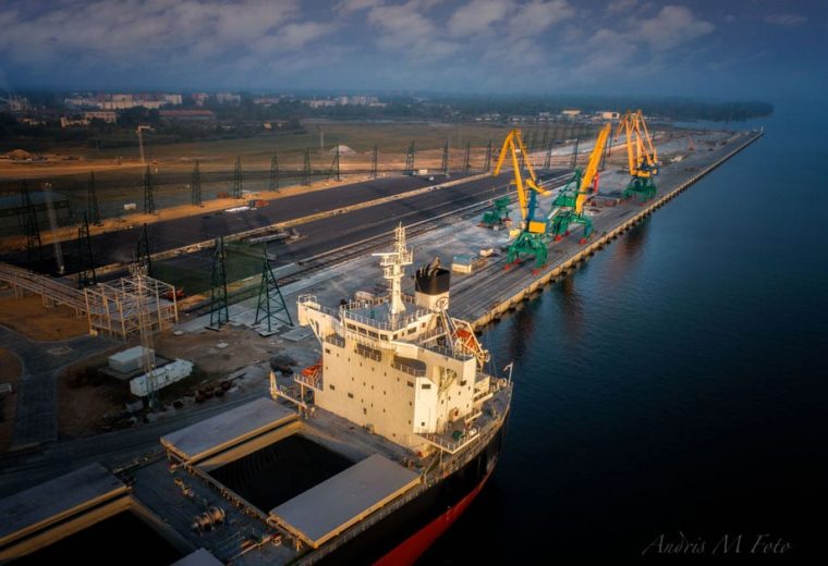 An aerial view of a cargo ship docked at an industrial port with cranes