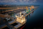 An aerial view of a cargo ship docked at an industrial port with cranes
