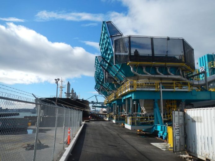 A fenced pathway leads to an industrial structure with teal and yellow components