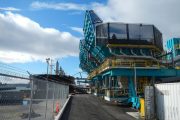 A fenced pathway leads to an industrial structure with teal and yellow components