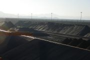Large piles of dark material with a crane and mountains in the background