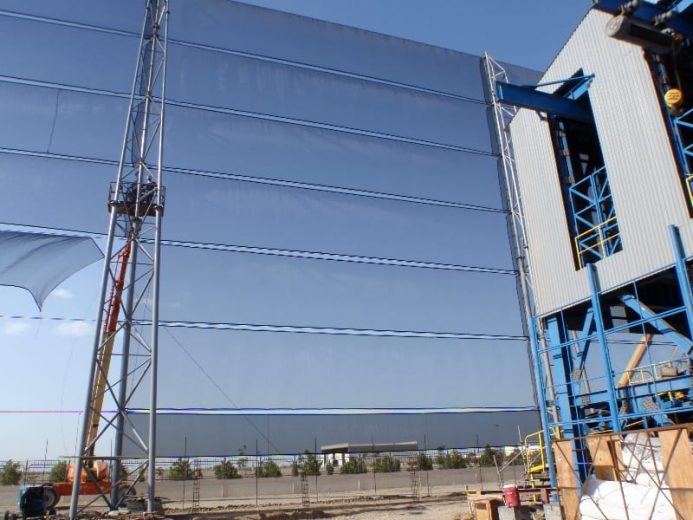 A large industrial wind fence with blue mesh panels supported by metal poles and a crane