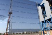 A large industrial wind fence with blue mesh panels supported by metal poles and a crane