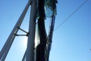 A person stands on a lift installing a green mesh netting on tall poles against a clear blue sky