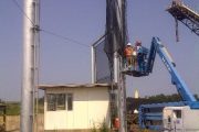 Construction workers install a large metal windbreak fence with a crane and lift